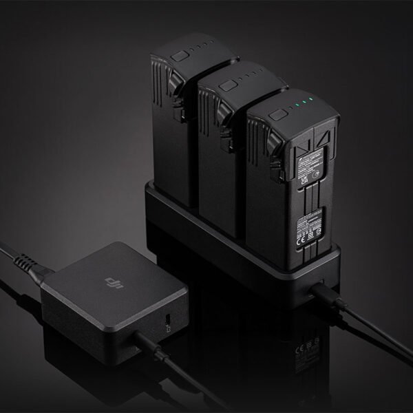 A black DJI 100W USB-C Power Adapter plugged into a wall outlet, with cables charging a drone battery
